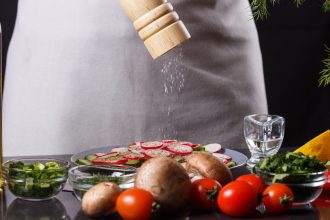 young woman in a gray apron seasoning salt cucumber and radish salad.